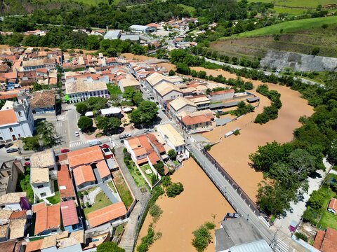 Vista a&eacute;rea por drone de uma enchente urbana, mostrando ruas alagadas, casas parcialmente submersas e o impacto das chuvas intensas. Conceito de desastre natural, mudan&ccedil;as clim&aacute;ticas, crise ambiental.