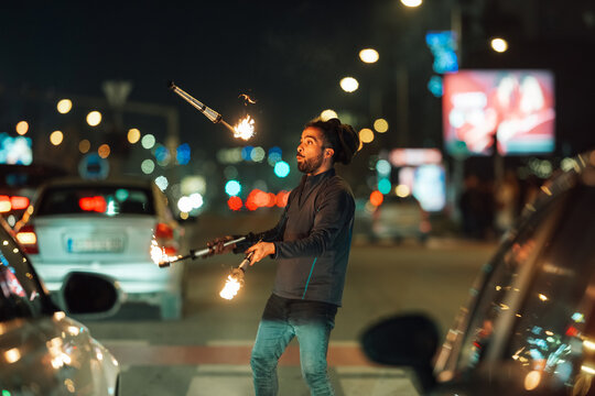 Man juggling fire sticks at night city street