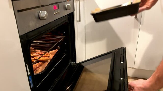 A man places a baking sheet with meat in the oven. Home cooking. Oven close-up.