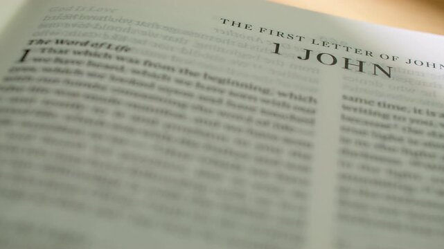 Bible pages flipping to 1 John letter book. Turning pages of the New Testament letter regarding love, light, and fellowship with God. 4K close up shot for religious study and scripture reading.