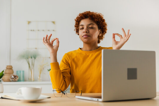 No stress keep calm. Mindful African businesswoman practices breathing exercises at home office. Peaceful young woman at workplace enjoy yoga eyes closed hands in chin mudra gesture. Office meditation