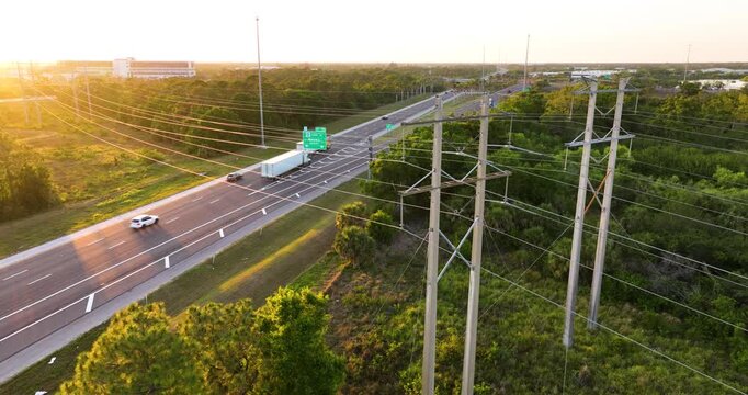 Aerial view of power lines on steel pylons stretching over multilane highway with flowing traffic. Electricity transmission infrastructure in urban area.