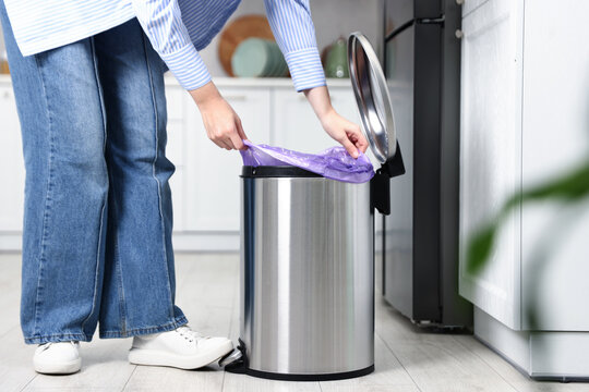Woman putting garbage bag into trash can in kitchen, closeup