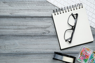 Office workplace. Computer keyboard, glasses and stationery on grey wooden desk, flat lay. Space...