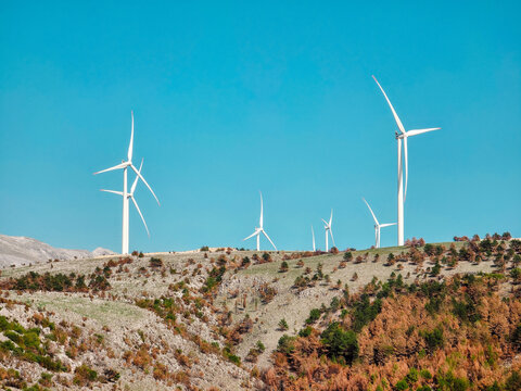 Wind turbines on a rocky mountain ridge under a clear blue sky near Mostar, Bosnia and Herzegovina. Renewable energy in a rural landscape.