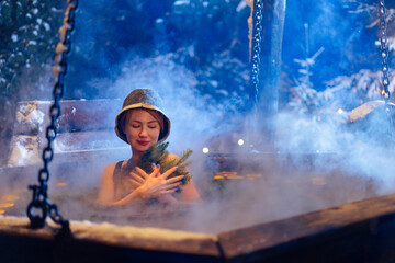 Caucasian female relaxing in winter hot tub with Citrus grapefruit, orange and evergreen spruce branches in snowy forest at night