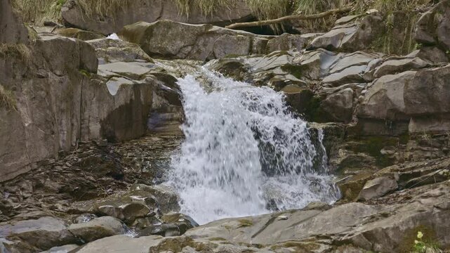 View of a detail of a small waterfall among rocks in the mountains. Water flowing with splashes through wet rocks and stones