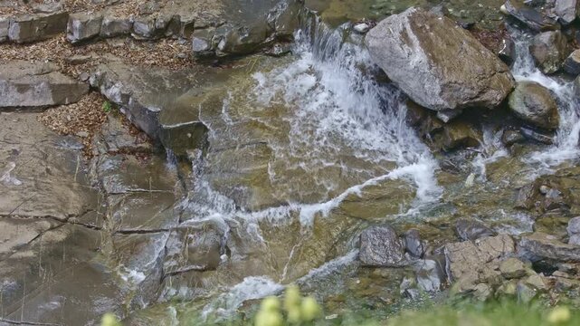 View of a detail of a small waterfall among rocks in the mountains. Water flowing with splashes through wet rocks and stones