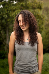 Naklejka premium Portrait of a cheerful female with natural look standing outdoors with a green blurred background, looking down with a shy and genuine smile.