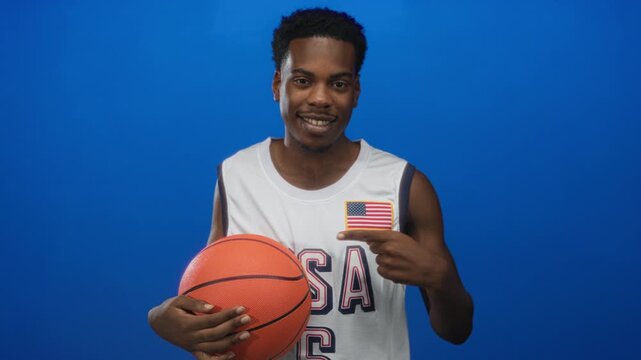 Man holding basketball points finger to flag patch on jersey in studio; patriotism unity sport spirit.