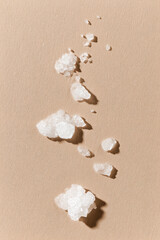 Close-up of Himalayan salt crystals scattered on a beige surface, showcasing the unique texture and shape of the salt for culinary or aesthetic use.