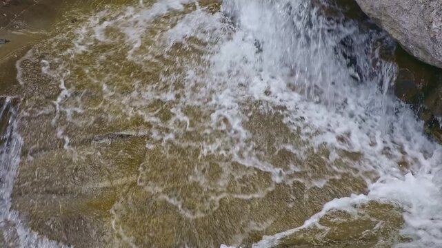 View of a detail of a small waterfall among rocks in the mountains. Water flowing with splashes through wet rocks and stones