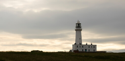 White Lighthouse on a Quiet Coastal Hill at Sunset Under Moody Cloudy Sky