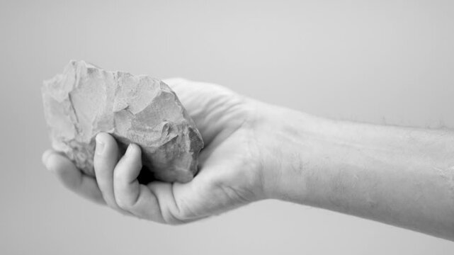 Hand Holding Paleolithic Biface Stone Tool, Prehistoric Flint Hand Axe Isolated on White Background. slow motion. black and white