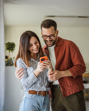 Smiling couple sharing content on smart phone at home