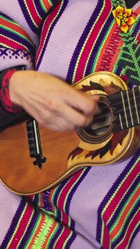 Close-up of a person wearing a colorful indigenous Andean poncho with beaded flower details, playing a traditional stringed instrument Charango guitar.