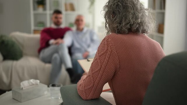 Female psychologist counseling male couple during therapy session
