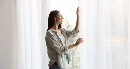 Fotobehang Karaktertjes Beautiful woman opening window curtains at home  © New Africa