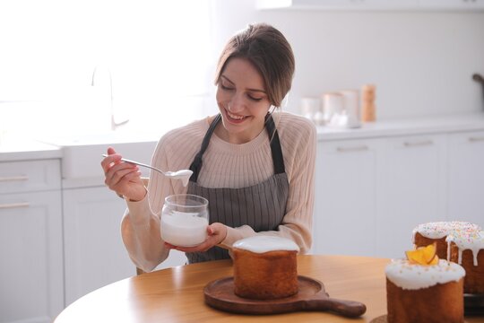 Young woman decorating traditional Easter cake with glaze in kitchen