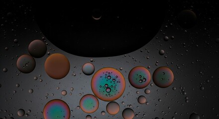 Iridescent oil droplets of various sizes floating on water against a dark background.