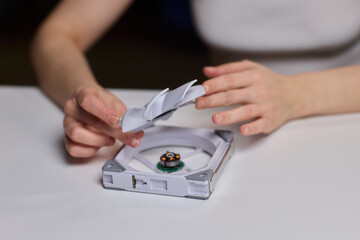 Detailed scene with technician disassembling small desktop fan carefully. Precise hands removing cover of desk fan during technical inspection with focused lighting