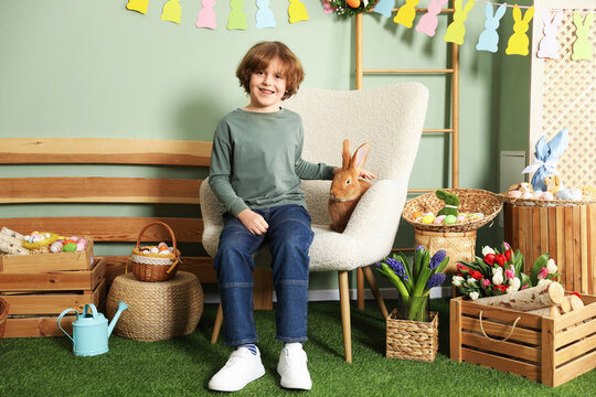 Little boy with cute Easter bunny in armchair indoors