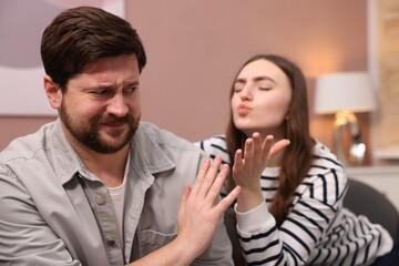 Naklejka premium Embarrassed man refusing kiss from young woman at home, selective focus