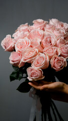 A florist creates a custom bouquet. Close-up of a bouquet of roses against a gray background. Beautiful pink roses at a flower shop.