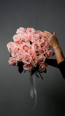 A florist creates a custom bouquet. Close-up of a bouquet of roses against a gray background. Beautiful pink roses at a flower shop.