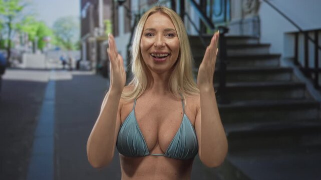 Woman wearing a blue bikini top with clasped hands praying in urban street scene near building staircase; hope.