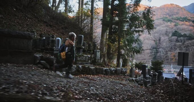 Little boy walking on autumn trail of Japanese graveyard in the morning - steady cam tracking shot