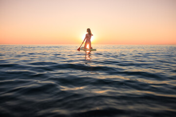 Fototapeta premium Young woman walking on stand up paddle sup boards by the sea during summer vacation
