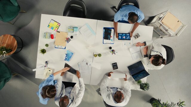 Top down view of diverse professionals collaborating in brainstorming session. Team shares medical expertise and diagnostic solutions for improved therapy at clinic.