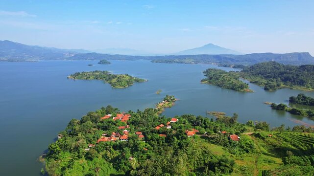 Aerial drone footage of a bay and peninsula, with some local houses, with the whole Jatigede reservoir behind and Tampomas volcano, in flat waters, in Sumedang regency, Java, Indonesia
