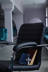 Fototapeta premium Christian cross pendant and books resting on a black leather chair in a waiting room
