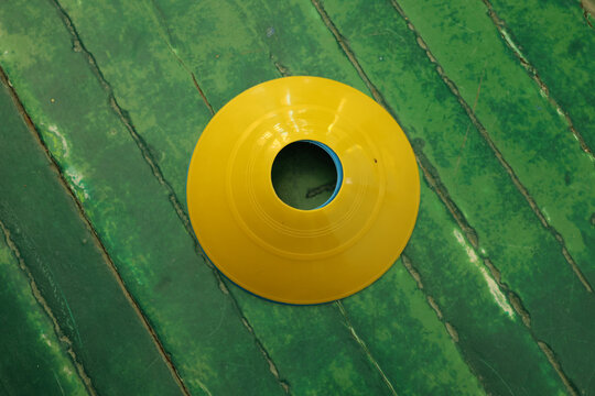 Bright yellow sports cone placed on a weathered green wooden surface with diagonal planks