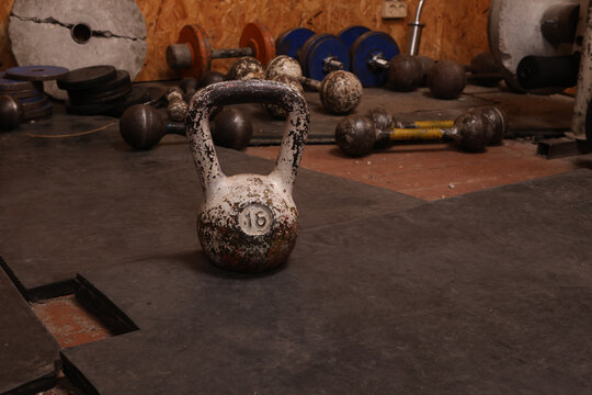 Old, worn kettlebell with weight marking sits on a gym floor surrounded by equipment