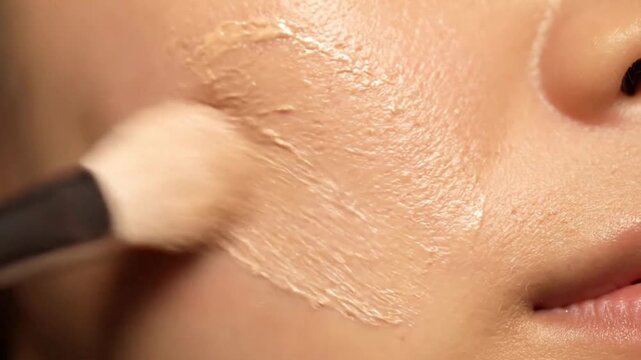Close-up of a cosmetic brush applying foundation to smooth skin.
