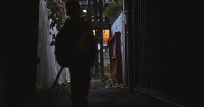 Mysterious shot of little boy with backpack walking through shadows of Japanese village alleyway and looking back