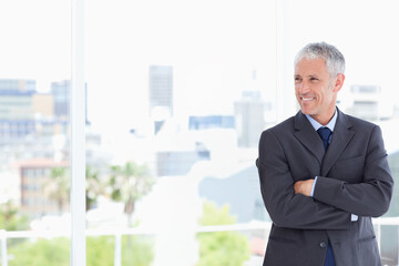 Mature man standing near floor-to-ceiling window in modern office, wearing suit and tie, copy space
