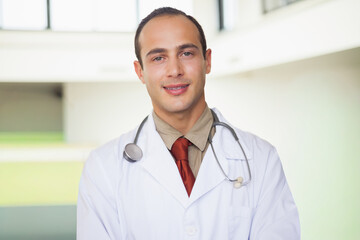 Male physician standing in medical facility lobby wearing white lab coat red tie stethoscope