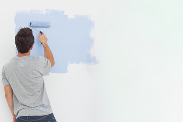Obraz premium Paint roller is painting light blue patch on white wall at left showing texture, copy space