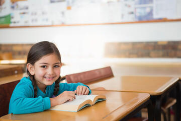 Child female student sitting in classroom at desk reading book, wearing turquoise top, copy space