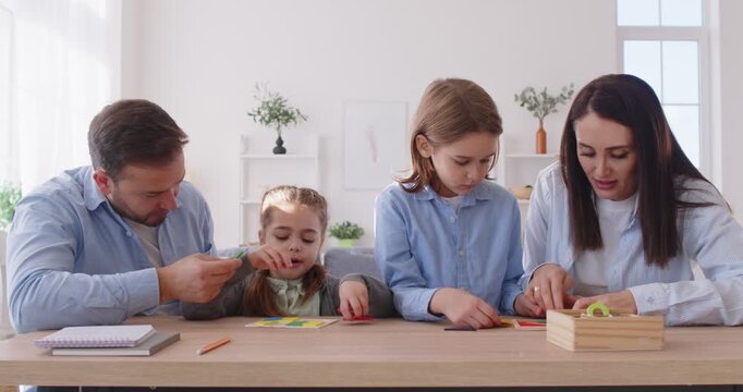 Happy family, parents and small children enjoy to play funny game, collect puzzle on desk, leisure activity, have fun at home, developing logical and fine motor skill, solving task, learning 
