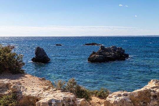 A rocky shoreline with clear blue water on Tabarca Island near Alicante. Several rock formations rise from the sea under a bright sky, creating a calm Mediterranean coastal landscape.
