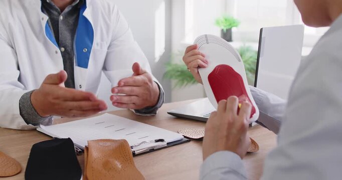 Orthopedist doctor shows orthopedic insoles to patient in medical clinic. They discuss custom orthotics and arch support to relieve foot pain. Concept medicine, foot healthcare and comfort.