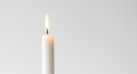Lit white candle against a blank backdrop, flame gently burning at the top