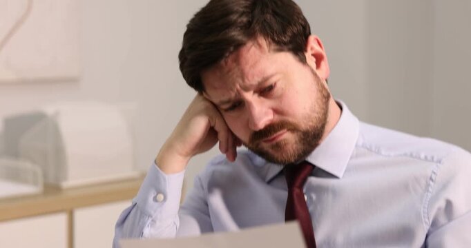 Unhappy businessman feeling fatigue at wooden table in office. Camera moving forward