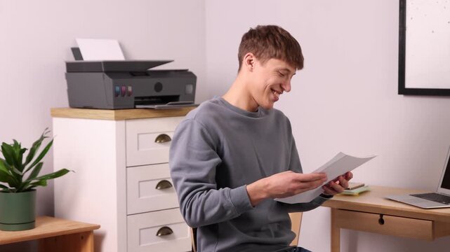 Smiling man using laptop and printer at table in office