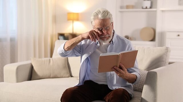 Unhappy senior man with book feeling fatigue at home